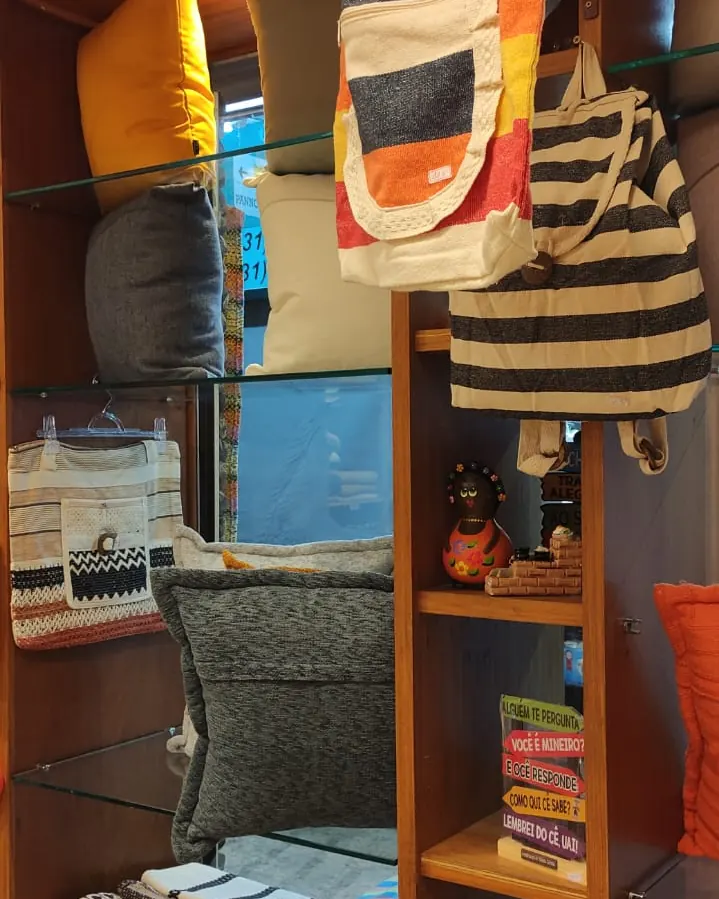 Canto da loja com sacolas de tecido penduradas, almofadas e panos dobrados
